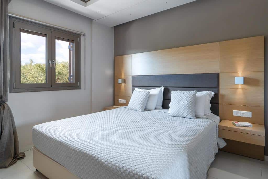 Quarto do Kymothoe Elite com uma cama de casal, uma estrutura de cabeceira com duas mesinhas e abajures presos, além de uma janela, para representar hotéis em Zakynthos