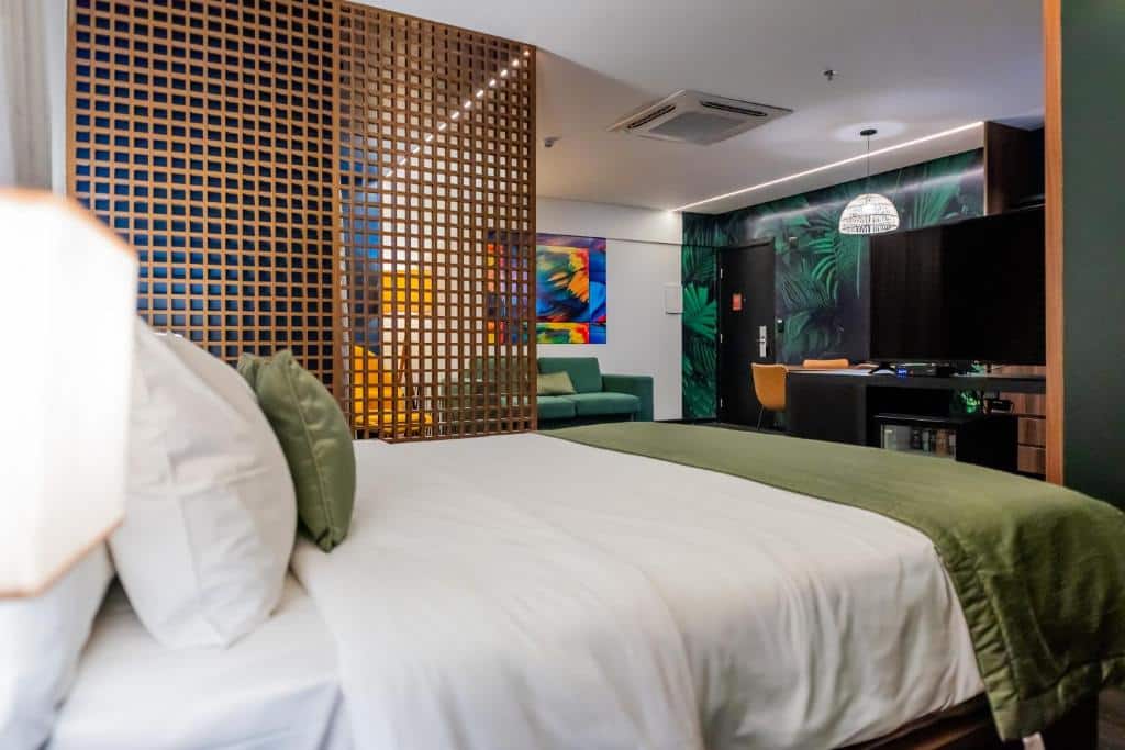 Quarto moderno no Mercure Belem Boulevard com uma cama, roupa de cama verde, uma divisória de madeira, arte na parede e uma área de trabalho ao fundo, para representar hotéis em Belém do Pará.