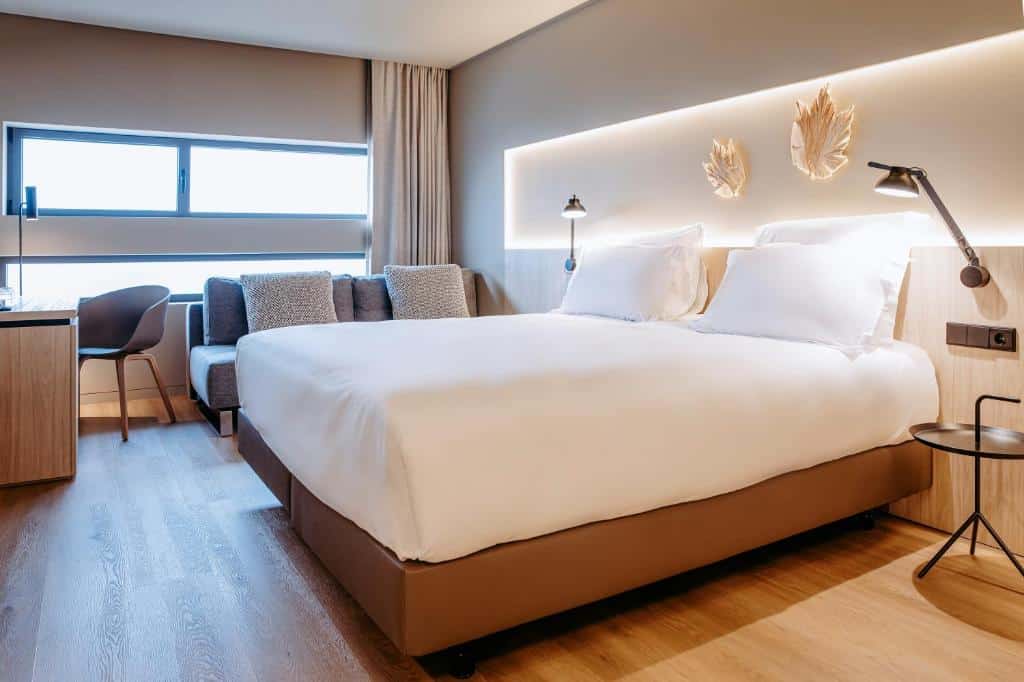 Quarto moderno do Mercure Fátima com uma cama de casal, sofá, escrivaninha, janela, luminárias de parede e decoração em tons neutros, para representar onde ficar em Fátima.