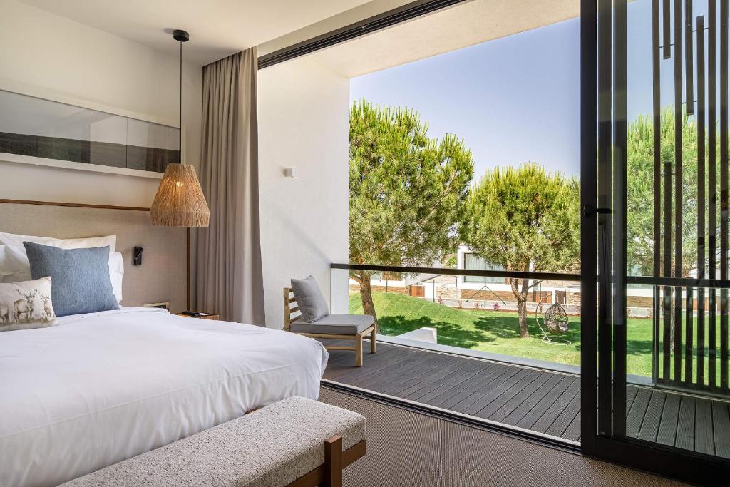 Quarto no Evora Farm Hotel & Spa com uma cama bem arrumada, cadeira e portas de varanda abertas com vista para árvores e uma área gramada do lado de fora, para representar onde ficar em Évora.