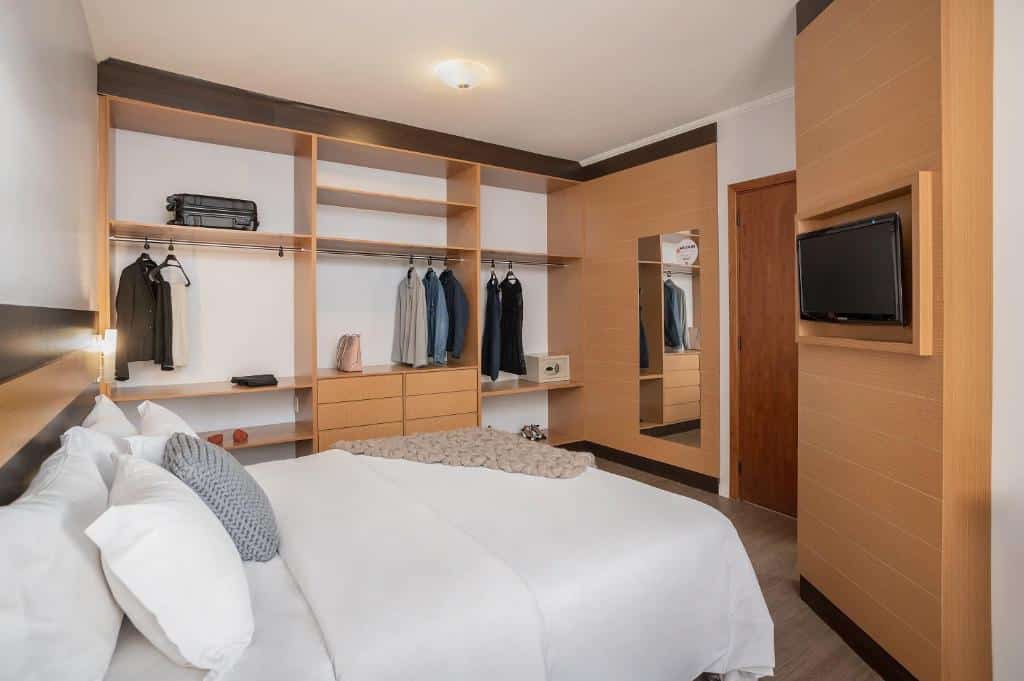 Um quarto no Piazza Navona com uma cama grande e armário aberto com cabides, além de um espelho de corpo inteiro e uma televisão na direção da cama.