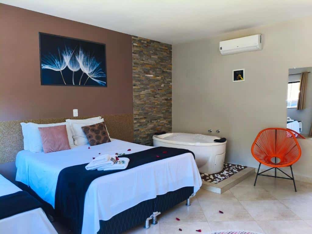 Quarto da Pousada Recanto da Cascata com duas camas, uma cadeira redonda laranja, uma banheira de hidromassagem e uma decoração moderna com arte na parede e um ar-condicionado, para representar pousadas em Águas de Lindóia.