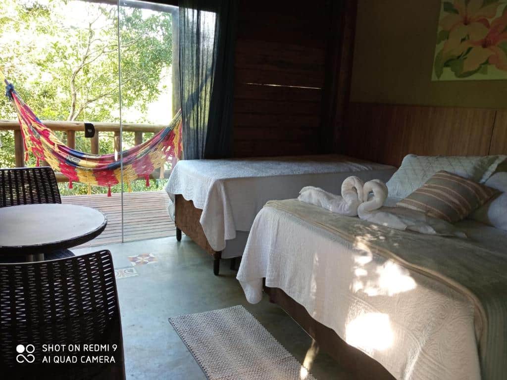 Um quarto com duas camas, uma mesa com cadeiras, um arranjo de toalhas e uma rede em uma varanda com vista para a vegetação, no Recanto Berço das Águas em Piraquara.