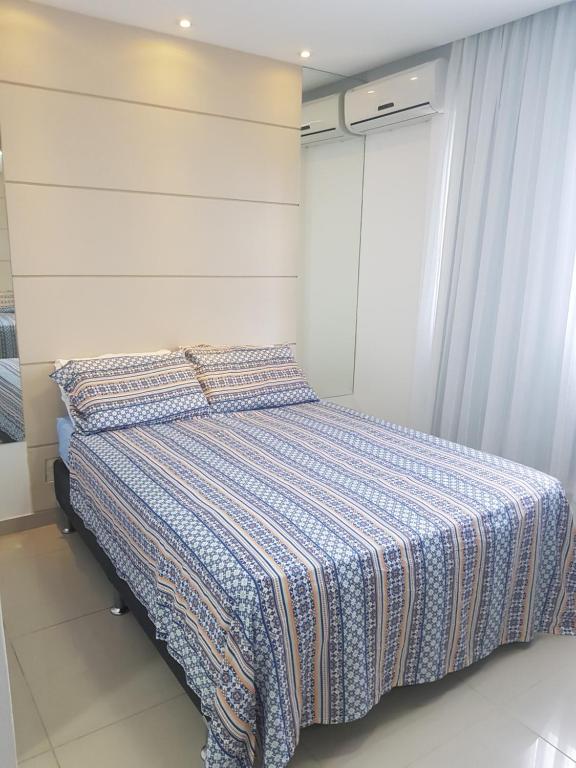 Uma cama bem arrumada no Rio Centro – Barra da Tijuca – Recreio – Praia com roupas de cama estampadas em um quarto moderno com paredes brancas, piso de azulejo e dois aparelhos de ar-condicionado, para representar airbnb na Barra da Tijuca.