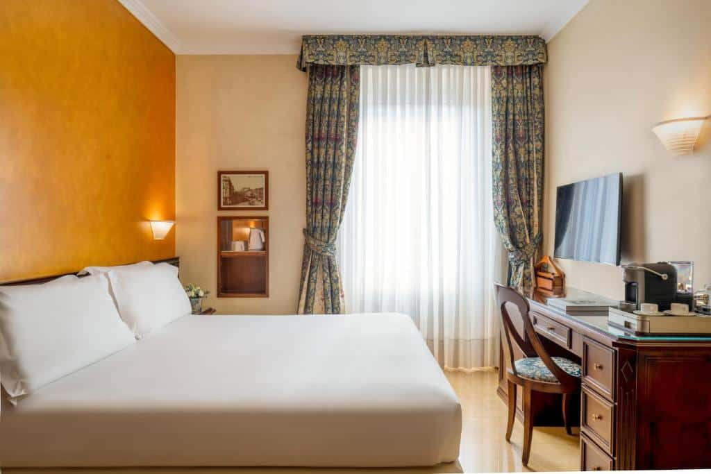Quarto no UNAHOTELS Galles Milano com uma cama de casal, escrivaninha com cadeira, TV na parede, janela com cortinas e paredes amarelas quentes, para representar hotéis Mercure em Milão.