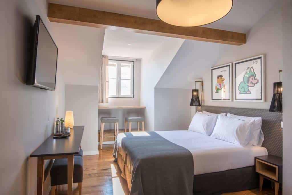 Quarto do Urbano FLH Hotels Lisboa com cama de casal, escrivaninha, TV na parede, duas banquetas ao lado de uma janela e arte emoldurada acima da cama, para representar melhores hotéis em Lisboa.