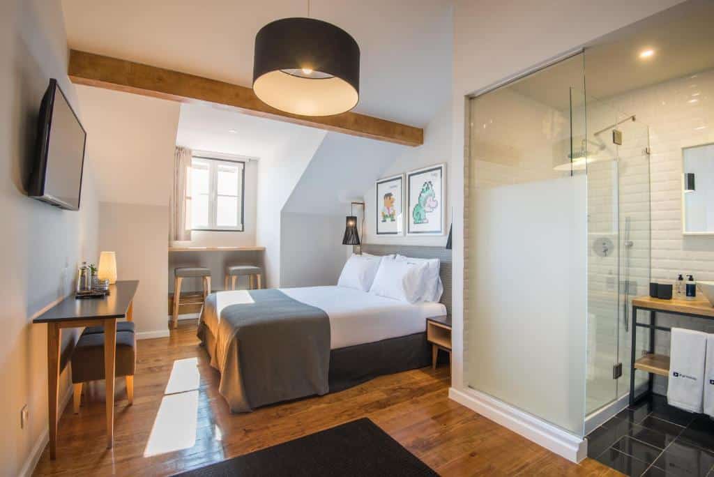 Quarto no Urbano FLH Hotels Lisboa com uma cama de casal, escrivaninha, TV na parede, janela e chuveiro com box de vidro no canto, para representar hotéis no Chiado em Lisboa.
