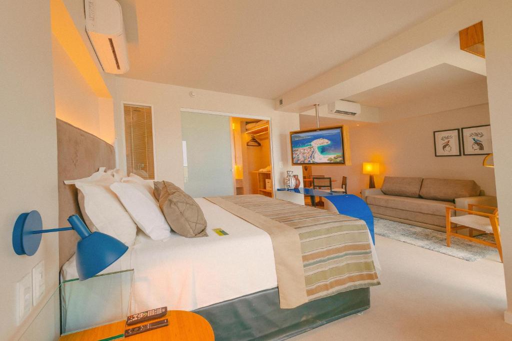 Quarto no Verdegreen Hotel na Praia de Manaíra, com uma cama de casal, sofá, TV, escrivaninha, luminárias de cabeceira e decoração neutra com detalhes em azul, para representar hotéis em João Pessoa.