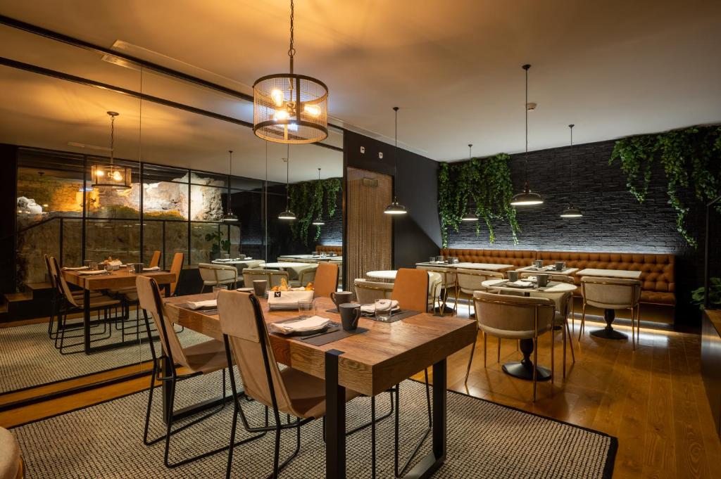Uma moderna área de jantar de restaurante, no Ferraria XVI FLH Hotels Lisboa, com mesas de madeira, cadeiras almofadadas, luzes pendentes e vegetação em paredes de tijolos pretos.