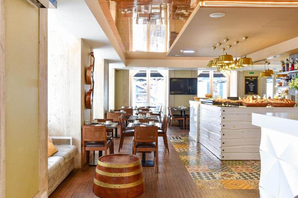 Interior luminoso no My Sotyr Hotel Ouro, de café com mesas de madeira, cadeiras, balcão de bar, luzes penduradas e violões decorativos na parede.