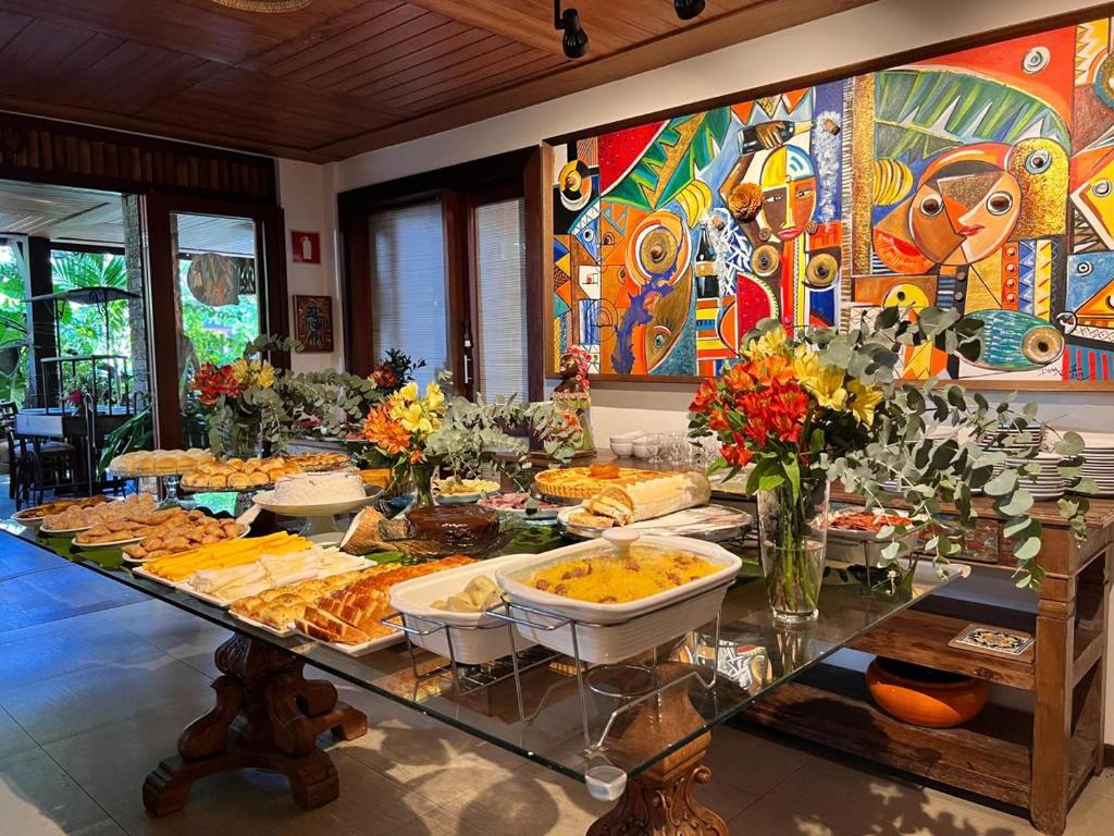 Uma mesa de vidro com vários pratos e flores em uma sala colorida com obras de arte abstratas na parede, na propriedade da Pousada João Sol na Praia do Forte.