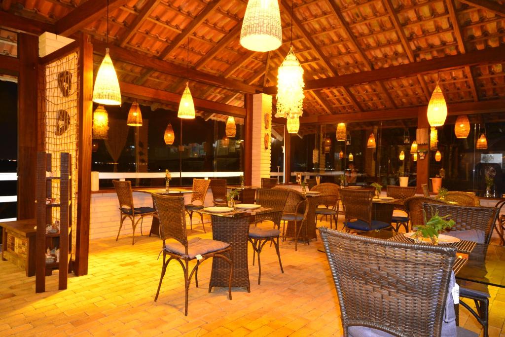 Restaurante ao ar livre com cadeiras de vime, mesas de madeira, luzes penduradas e um telhado de azulejos, iluminado calorosamente à noite, na Villa dos Ganchos Hospedaria.