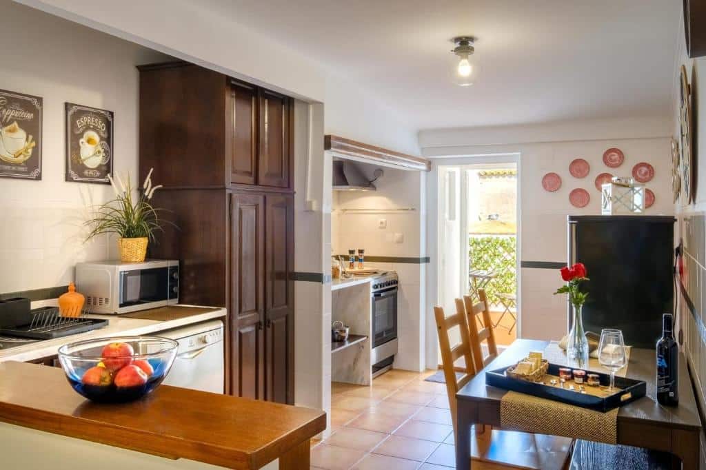 Uma cozinha no Almoura Giraldo Centro Histórico com armários de madeira escura, uma mesa de jantar para duas pessoas, uma tigela de maçãs e arte na parede acima de um micro-ondas, para rrepresenta onde ficar em Évora.