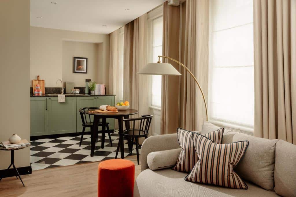 Uma pequena cozinha e sala de jantar com armários verdes, uma mesa com cadeiras e um sofá em uma sala de estar de tons neutros, no Native Kings Wadrobe, St Pauls.