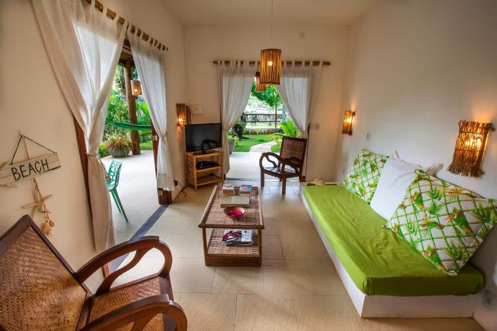 Uma sala de estar bem iluminada com móveis de vime, um sofá verde, TV e janelas grandes que se abrem para um pátio com jardim, no Paradise Beach House.