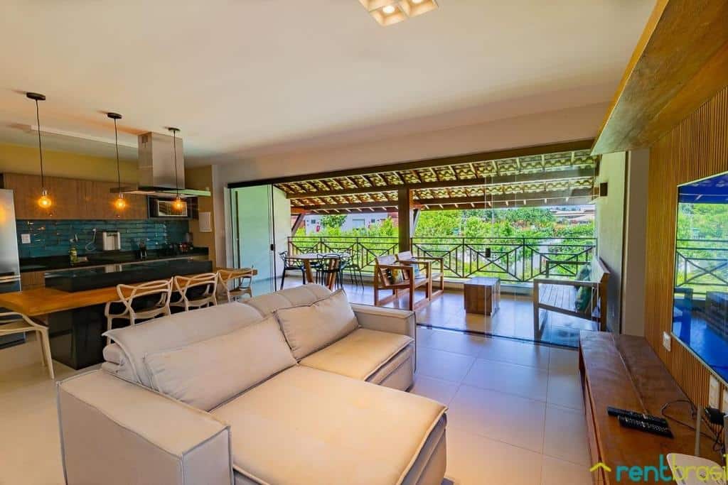 Sala de estar e cozinha em plano aberto com sofá, área para refeições e ampla varanda com vista para a vegetação, no Ykutiba Imbassaí - Apartamento 3 Quartos Superior - I104.