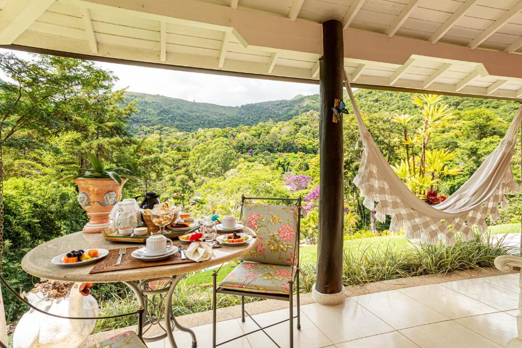 Pátio externo com uma mesa de café da manhã, cadeiras floridas, rede e uma vista verdejante da montanha ao fundo, no Su Paradise Villa e Chalés.