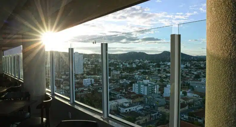 A luz do sol brilha em uma varanda no Dubai Suites, com vista para uma paisagem urbana com prédios, colinas e um céu parcialmente nublado, para representar hotéis em Montes Claos.
