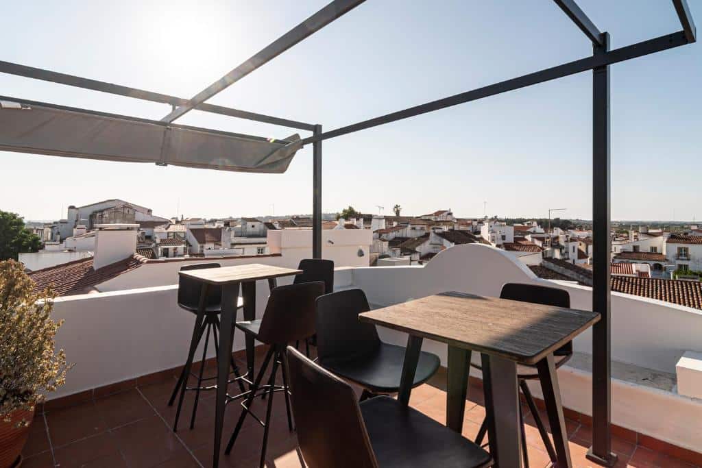 Um terraço na cobertura com mesas, cadeiras, uma estrutura de pérgola e uma vista de edifícios brancos sob um céu claro, no Templo Boutique Hotel.