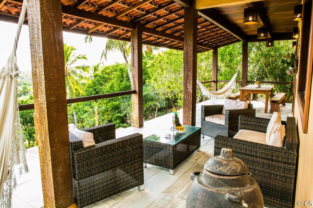 Pátio coberto com cadeiras de vime, mesa de centro de vidro, rede e mesa de jantar de madeira com vista para árvores verdejantes, na propriedade da Pousada Too Cool em Diogo.