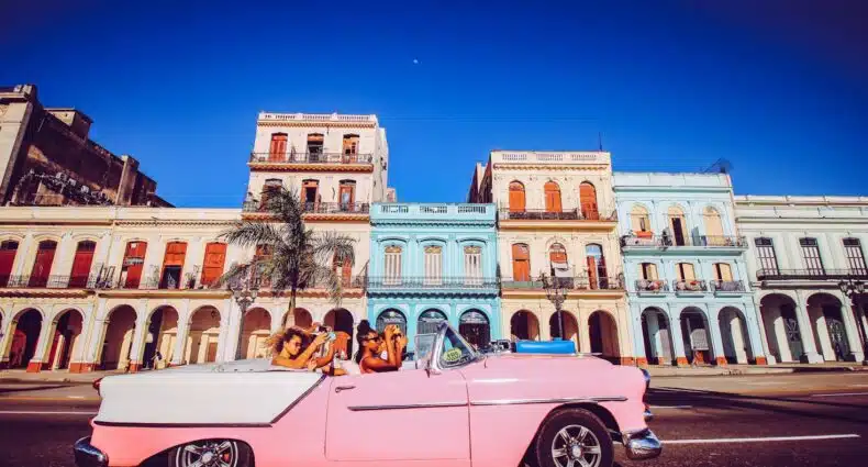 Um carro conversível clássico rosa passa por prédios históricos coloridos sob um céu azul claro que pode ser aproveitando com o eSIM Cuba.