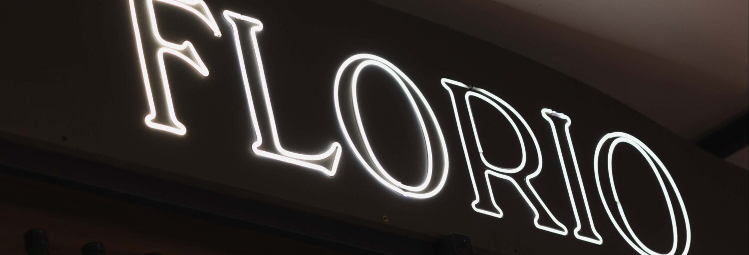 Letreiro luminoso com a palavra "FLORIO" em letras maiúsculas grandes e brancas em um fundo escuro. Imagem para ilustrar post sobre degustação de vinhos no bairro de La Boca.
