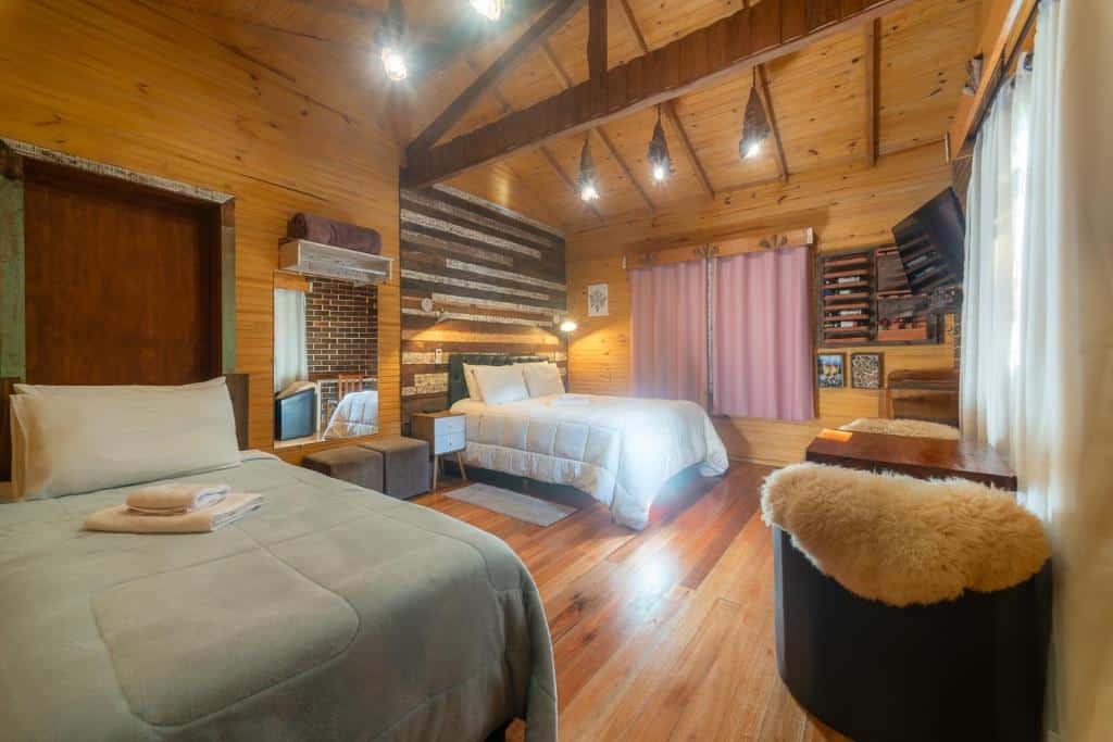 Um quarto rústico com paredes e teto revestidos de painéis de madeira, duas camas, uma TV, cortinas e um pequeno banco com uma capa de pele, na Pousada Caminhos da Natureza em Urubuci.