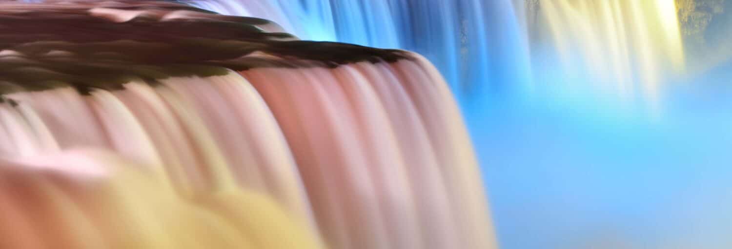 Uma imagem desfocada e em close-up de uma cachoeira com tons suaves de rosa, azul e amarelo se misturando.