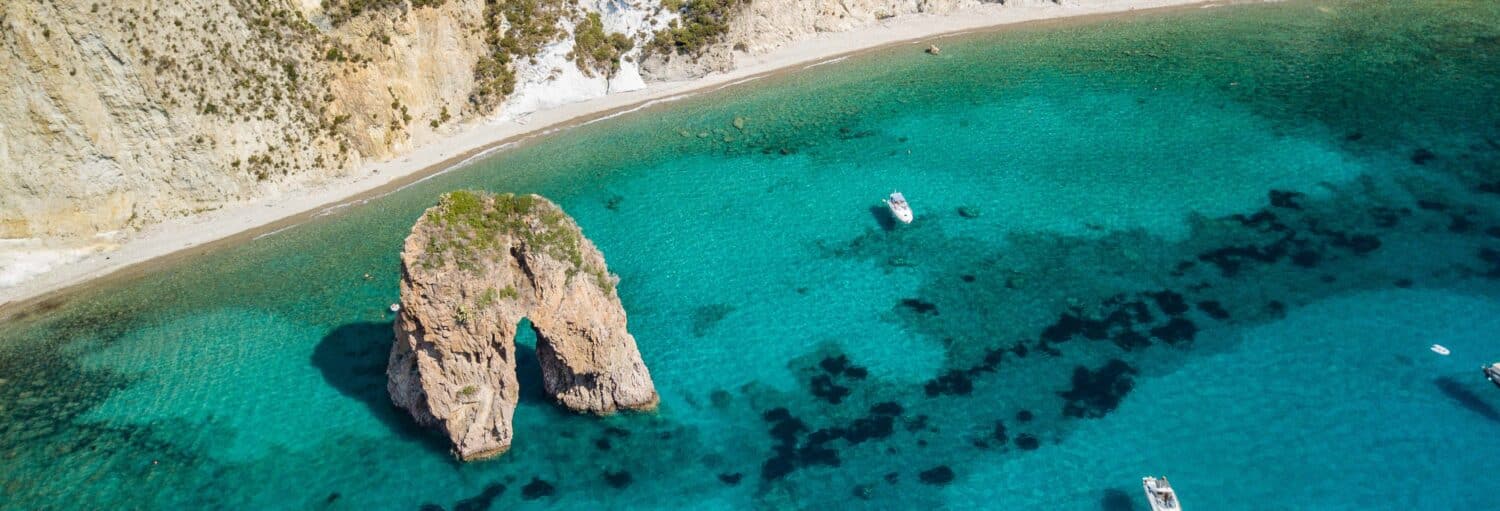 Vista aérea de um arco marinho rochoso próximo a um litoral arenoso com água azul-turquesa clara e vários barcos pequenos na Excursão a Ponza e passeio de barco