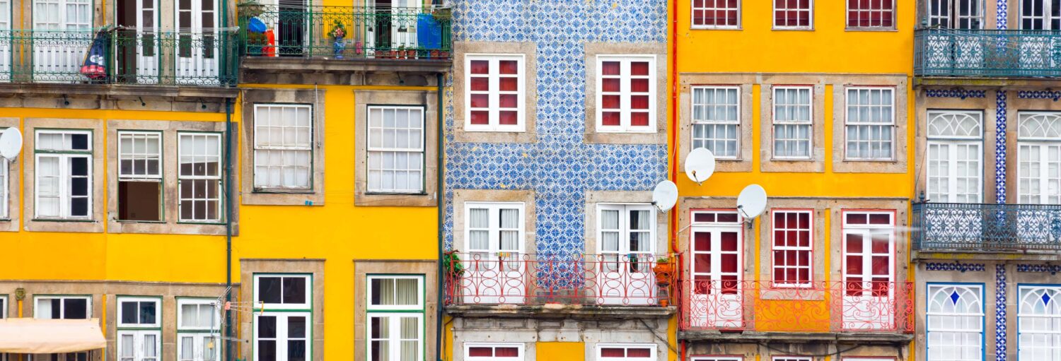 Uma fileira de edifícios coloridos com paredes amarelas e azulejos azuis padronizados, com varandas e janelas decoradas em vermelho. A foto é capa do post sobre o Free tour pela Cidade Velha do Porto.