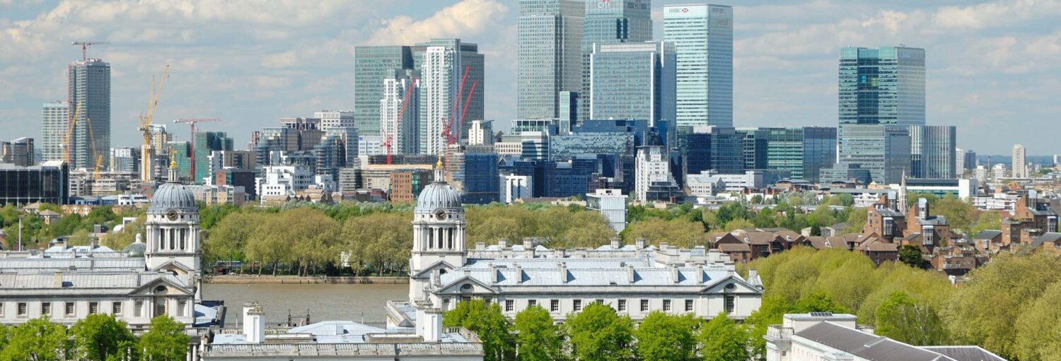 Vista de uma cidade com varios prédios, árvores e um rio no primeiro plano, onde há embarcações. Free tour por Greenwich