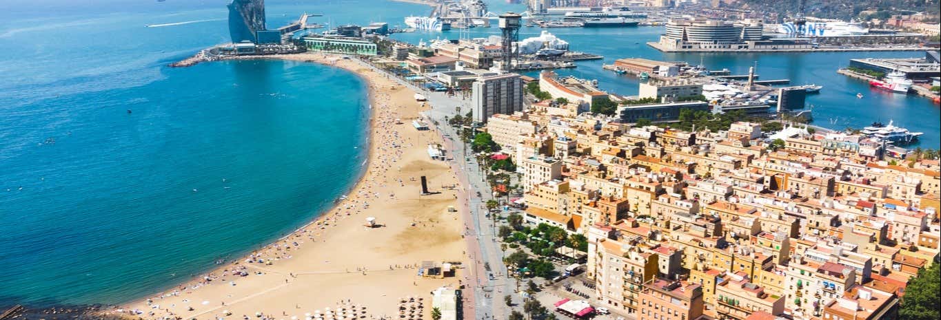 Vista aérea de uma praia de areia, edifícios da cidade e um porto com navios e barcos atracados ao longo da costa. A imagem ilustra o post sobre Free tour: La Barceloneta + Parc Ciutadella.