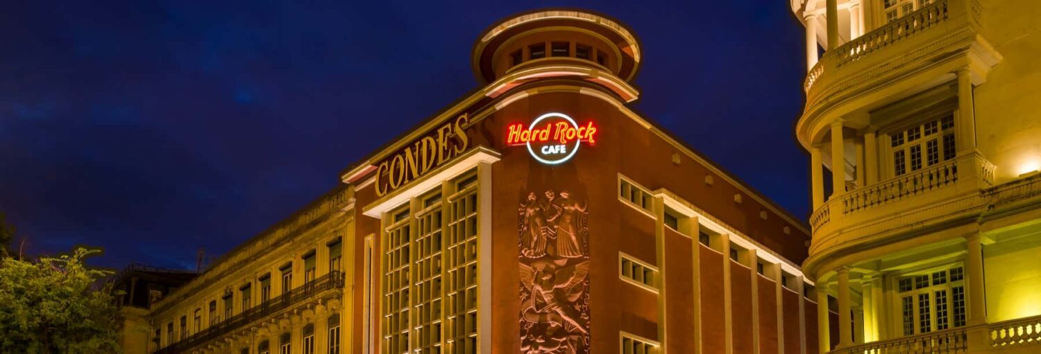 Vista externa do Hard Rock Cafe à noite, com letreiro de neon e edifícios históricos ao redor. Imagem para ilustrar post sobre Hard Rock Cafe Lisboa sem filas.