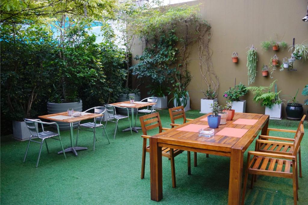 Área de jantar externa com mesas de madeira, cadeiras de metal, grama artificial verde e plantas ao longo de uma parede marrom, na propriedade do 474 Buenos Aires Hotel.