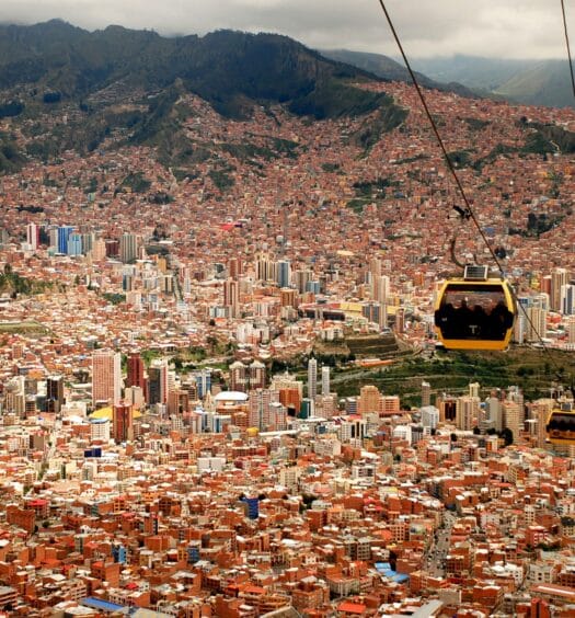 Teleféricos amarelos passam por La Paz, densamente construída com montanhas ao fundo e um céu nublado. A foto é capa do post de eSIM La Paz.