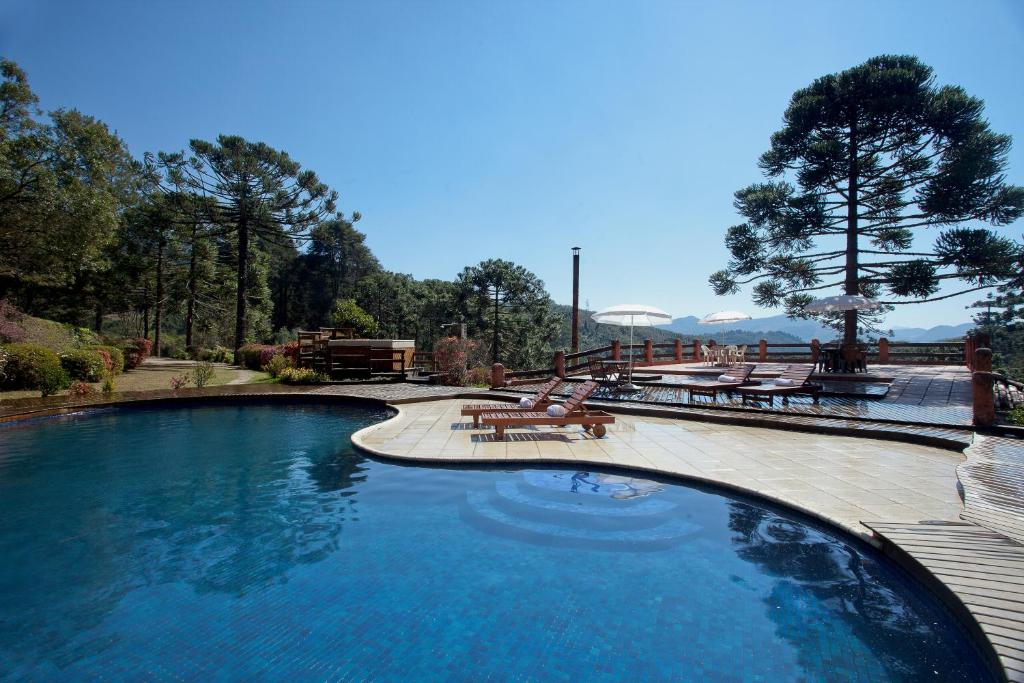 Piscina ao ar livre com espreguiçadeiras, deck de madeira, guarda-sóis e árvores altas sob um céu azul claro em uma área panorâmica, na propriedade do Hotel Fazenda Itapuá.