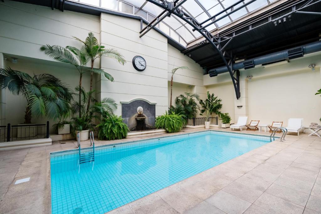 Área da piscina interna com água azul clara, espreguiçadeiras, palmeiras, um relógio e um teto de vidro, na propriedade do Loi Suites Recoleta Hotel, para representar hotéis em Buenos Aires.