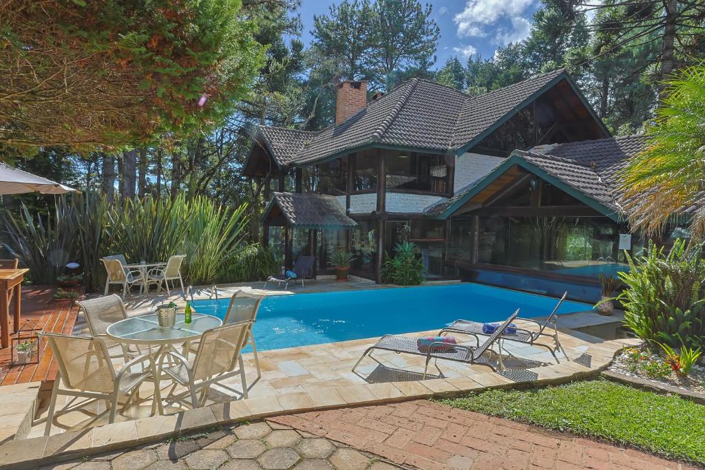 Uma casa moderna com telhado inclinado é vista atrás de uma piscina, móveis de pátio e árvores sob um céu parcialmente nublado, na propriedade da Pousada Cantos e Contos.