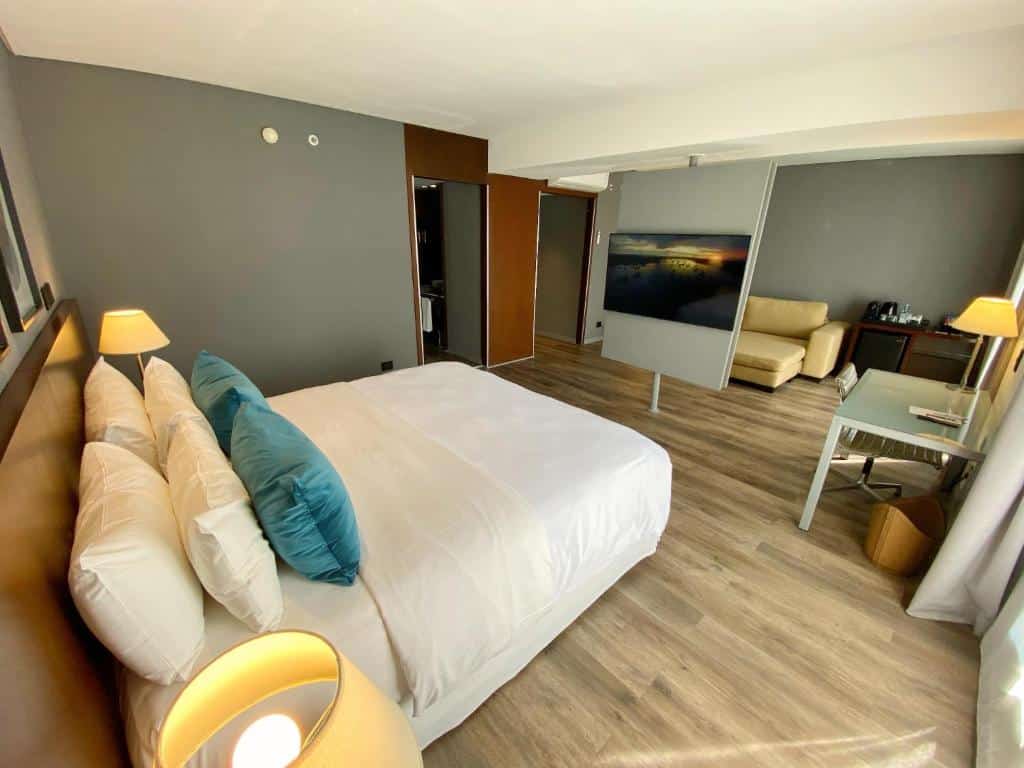 Quarto no 474 Buenos Aires Hotel com uma cama bem arrumada, escrivaninha, sofá, luminárias e piso de madeira em tons neutros, para representar hotéis peto da Casa Rosada em Buenos Aires.