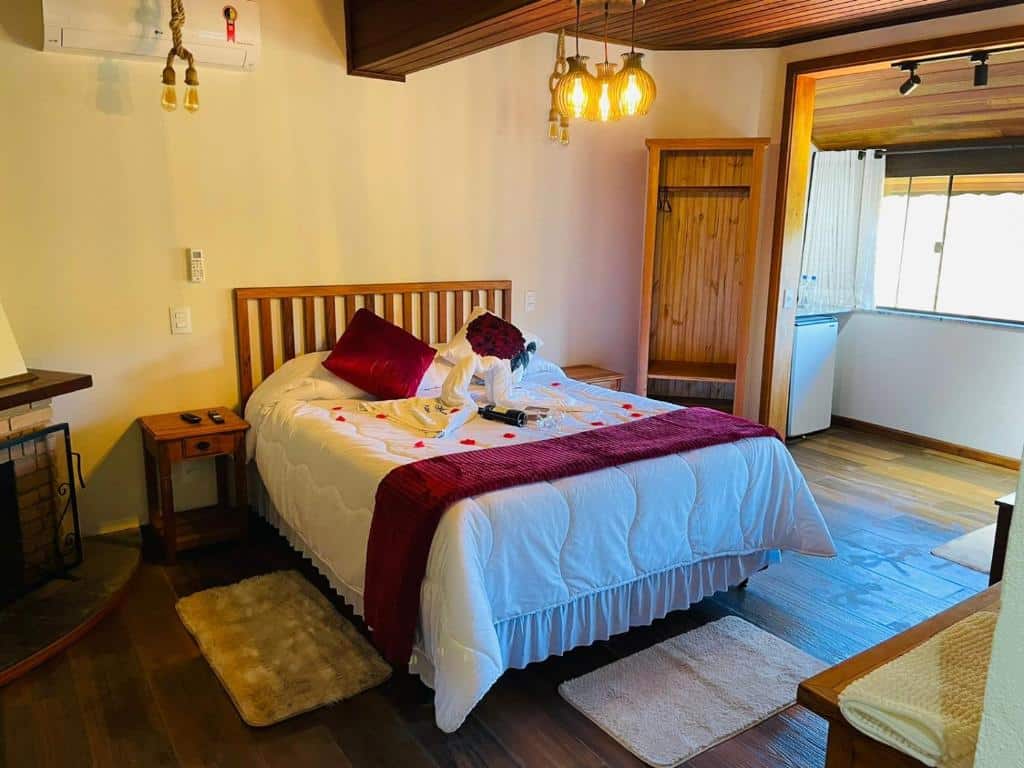 Uma cama bem arrumada com detalhes em vermelho e toalhas dispostas como cisnes em um quarto de madeira aconchegante com luz natural, no Hotel Pião Mineiro, para representar hotéis em Monte Verde.