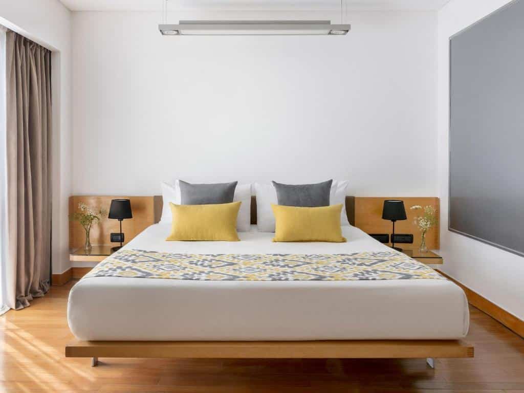 Quarto minimalista no HTL Urbano com uma cama grande, travesseiros amarelos e cinza, duas mesas de cabeceira, luminárias e um corredor de cama estampado, para representar hotéis perto da Casa Rosada em Buenos Aires.
