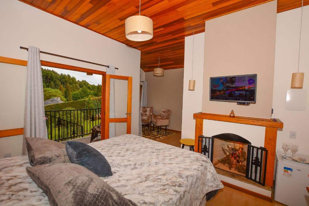 Um quarto aconchegante com camas de solteiro, lareira, TV na parede e uma varanda com vista para a vegetação, na Pousada Cantinho de Monte Verde.