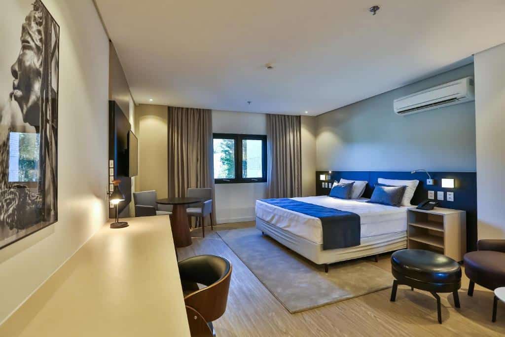 Quarto do Quality Hotel Blumenau com uma cama de casal, escrivaninha, cadeira, mesa pequena, janela, arte na parede e decoração neutra, para representar hotéis em Blumenau.