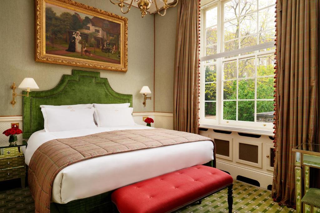 Uma cama bem arrumada com cabeceira verde, banco vermelho e uma grande janela em um quarto de estilo clássico, no The Montague On The Gardens, para representar onde ficar em Londres.