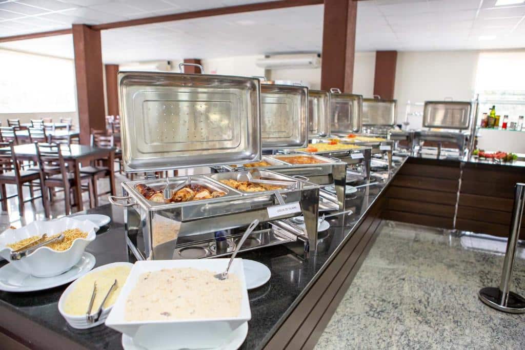 Uma mesa de bufê com vários pratos quentes e tigelas de acompanhamentos em um restaurante, servido no Hotel Zandoná.