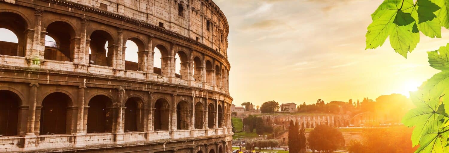 O Coliseu de Roma ao pôr do sol, com a luz do sol brilhando através de seus arcos e folhas verdes em primeiro plano no Go City: Roma Explorer Pass
