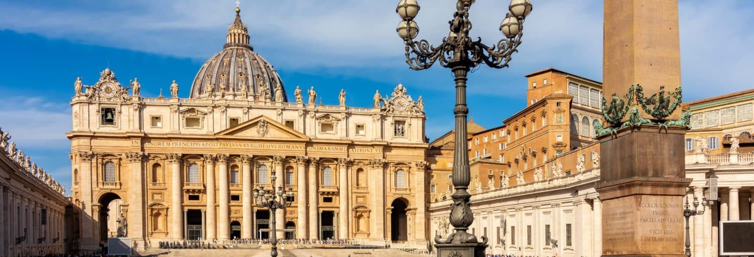 A Basílica de São Pedro com sua cúpula, um obelisco e postes de iluminação ornamentados na Cidade do Vaticano, sob um céu azul claro na Visita guiada pela Basílica de São Pedro