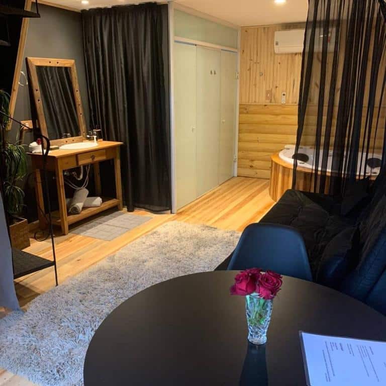 Uma sala aconchegante com uma mesa redonda, vaso de rosas vermelhas, penteadeira, sofá, tapete e banheira de hidromassagem, com painéis de madeira.