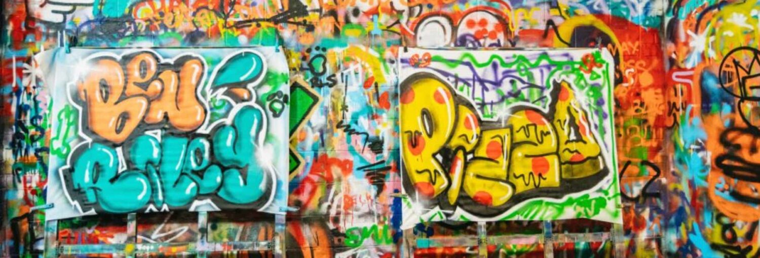 Parede de grafite colorida com duas marcas proeminentes em azul e amarelo, cercadas por vários desenhos de tinta spray sobrepostos.