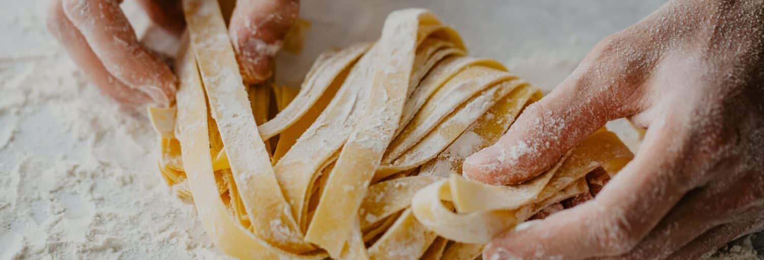 Com as mãos polvilhadas de farinha, manuseie um feixe de macarrão cru e plano em uma superfície enfarinhada no Aula de massa italiana e tiramisu